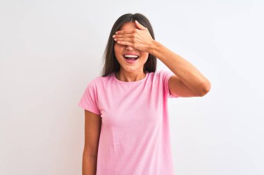 İzole edilmiş beyaz arka plan üzerinde pembe günlük tişört giyen genç ve güzel bir kadın. Gülümsüyor ve elleri yüzünde şaşkınlıktan gözleri kapatıyordu. Kör kavram.