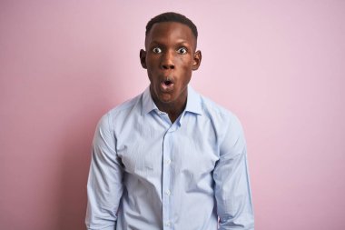 Mavi şık gömlekli Afro-Amerikan bir adam pembe arka planda dikiliyor korku, korku ve heyecan dolu bir yüz ifadesinden korkuyor ve şok oluyor..