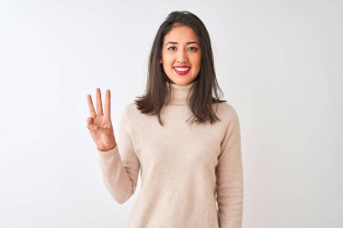 Balıkçı yaka kazak giyen güzel Çinli kadın izole edilmiş beyaz arka plan üzerinde duruyor ve üç numaralı parmaklarıyla işaret ederken kendinden emin ve mutlu bir şekilde gülümsüyor..