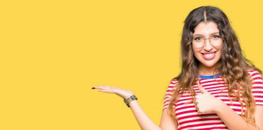 Gösteren palm el ve yukarıya, mutlu ve neşeli gülümseyen baş parmakları Tamam jest yapıyor giyen genç güzel kadın gözlük