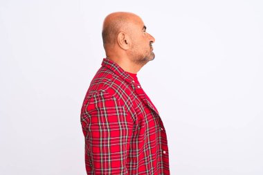 Orta yaşlı yakışıklı bir adam, günlük gömleğini giymiş, izole edilmiş beyaz arka planda duruyor, yan tarafa bakıyor, rahat bir görünüm sergiliyor, kendine güvenen bir gülümsemeyle doğal bir yüz ifadesi var..