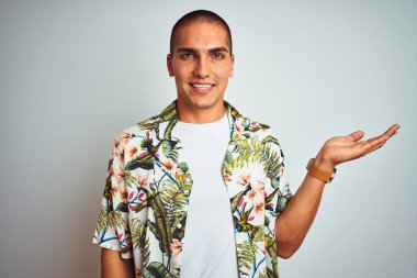 Tatilde beyaz arka planda Hawaii gömleği giymiş neşeli bir şekilde gülümseyen ve avuç içi kameraya bakan genç yakışıklı bir adam..