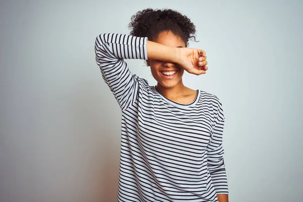 African american woman wearing navy striped t-shirt standing over isolated white background covering eyes with arm smiling cheerful and funny. Blind concept.