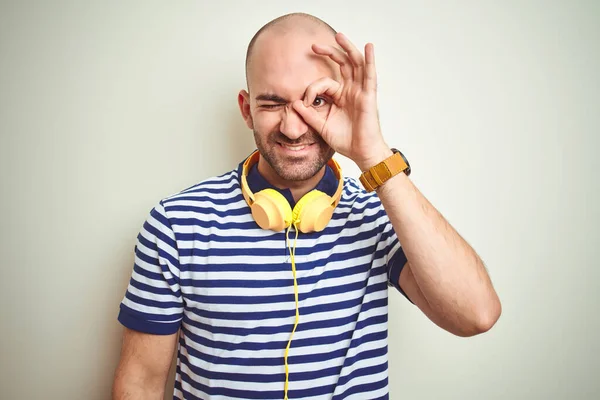 孤立した背景の上に黄色のヘッドフォンを着用して音楽を聴いている若い男は 手の笑顔でOkジェスチャーを行い 幸せな顔で指を通して目を見て — ストック写真