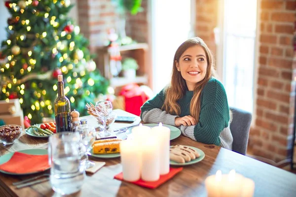 若い美しい女性の自宅でクリスマスツリーの周りの食品を食べるの横に顔を笑顔で 自然な表現を探して座っている 自信を持って — ストック写真