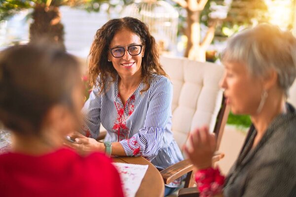 Meeting of middle age women having lunch and drinking coffee. Mature friends smiling happy using smartphone at home on a sunny day