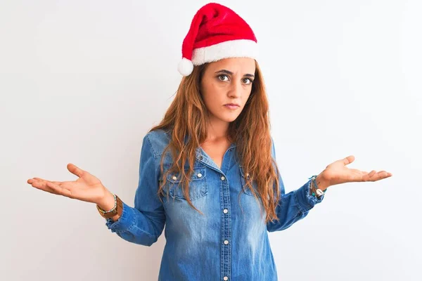 孤立した背景にクリスマスの帽子をかぶっている若い美しい赤毛の女性は 腕や手で上げられた混乱した表情 疑いの概念 — ストック写真