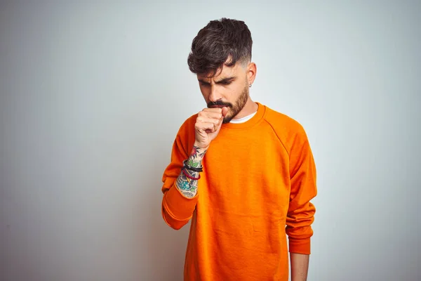 孤立した白い背景感の上に立ってオレンジセーターを着て入れ墨を持つ若い男は具合が悪く 風邪や気管支炎の症状として咳 医療の概念 — ストック写真