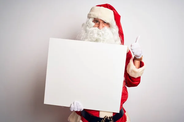 中年男人穿着圣诞老人的服装 举着横幅遮掩在孤独的白色背景上 开心地笑着做着好的手势 用手指竖起大拇指 很好的标志 — 图库照片