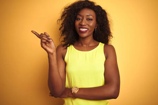 カメラを見ている側に手と指で指して 顔に大きな笑顔で孤立した黄色の背景の上に立ってTシャツを着て若いアフリカ系アメリカ人女性 — ストック写真