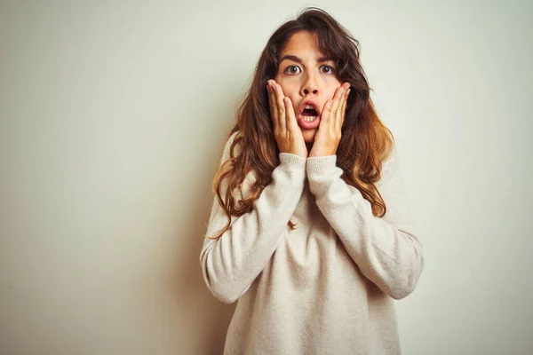 Young beautiful woman wearing winter sweater standing over white isolated background afraid and shocked, surprise and amazed expression with hands on face