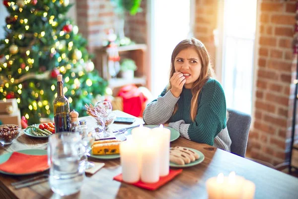 若い美しい女性の自宅でクリスマスツリーの周りに食べ物を食べて座っているストレスと口の爪をかむ上で手で緊張している 不安の問題 — ストック写真