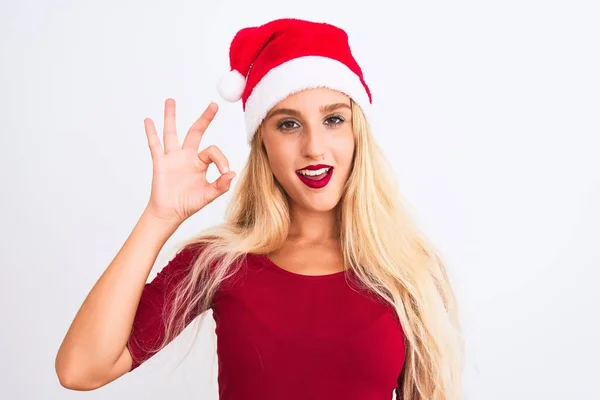 年轻美丽的女人戴着圣诞圣诞礼帽 站在孤独的白色背景上 微笑着积极地做着 手指手画脚地签了名 成功表达 — 图库照片