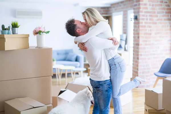 Young beautiful couple with dog hugging at new home around cardboard boxes