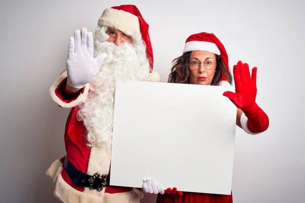 上了年纪的夫妇 身穿圣诞老人服装 举着横幅 高高地挂在孤独的白色背景上 张开双手 用严肃而自信的表情和防守的手势 做着停止的手势 — 图库照片