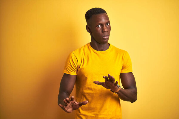Young african american man wearing casual t-shirt standing over isolated yellow background Moving away hands palms showing refusal and denial with afraid and disgusting expression. Stop and forbidden.