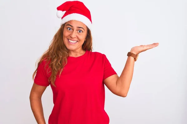 中年成熟しました女性身に着けていますクリスマス帽子上の隔離された背景笑顔陽気なプレゼンテーションとポインティングとともに手のひらカメラを見て — ストック写真