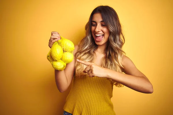 Молодая Красивая Женщина Держащая Сеть Лимонов Желтом Изолированном Фоне Счастлива — стоковое фото
