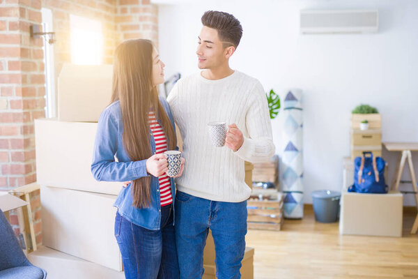 Young asian couple drinking a cup of coffee at new home, smiling happy around cardboard boxes from moving