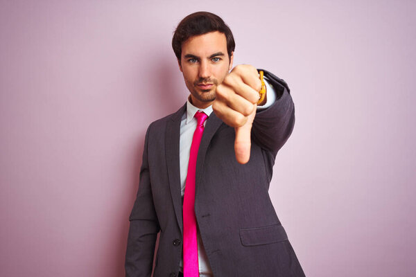 Young handsome businessman wearing suit and tie standing over isolated pink background looking unhappy and angry showing rejection and negative with thumbs down gesture. Bad expression.