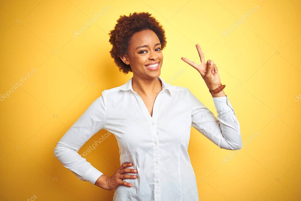 African american business woman over isolated yellow background smiling looking to the camera showing fingers doing victory sign. Number two.