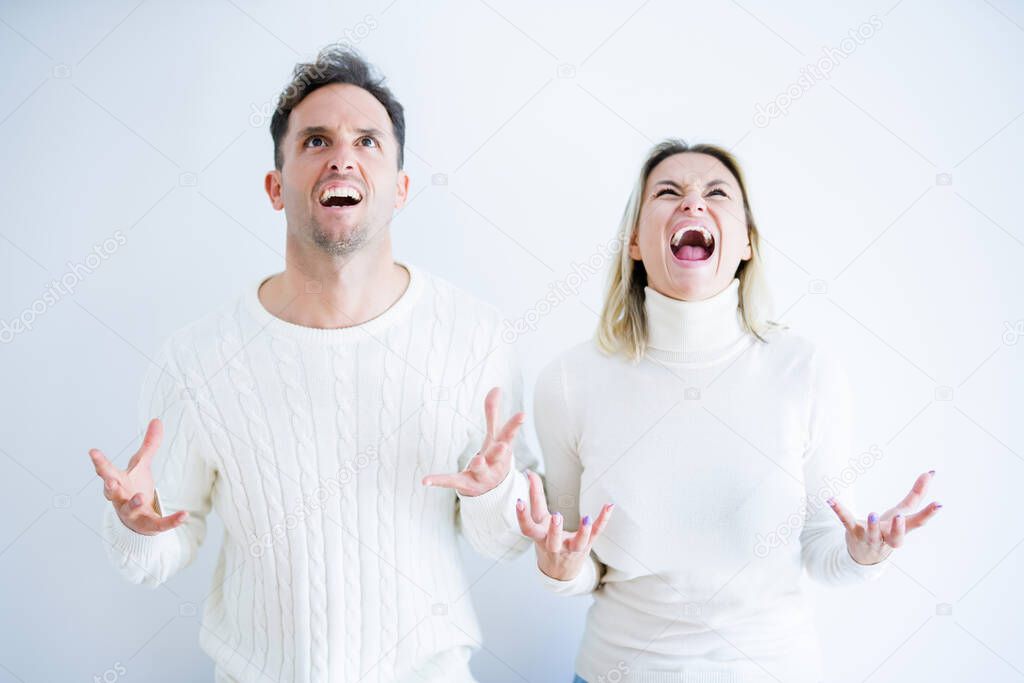 Young beautiful couple wearing casual t-shirt standing over isolated white background crazy and mad shouting and yelling with aggressive expression and arms raised. Frustration concept.