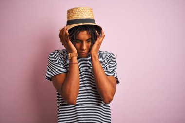 Siyah tişörtlü ve şapkalı Afro-Amerikan bir adam izole edilmiş pembe arka planda acı ve migrenden dolayı çaresiz ve stresli bir şekilde acı çekiyor. Ellerini başının üstüne koy..