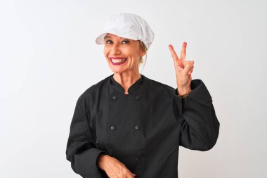 Üniformalı ve şapkalı orta yaşlı bir aşçı kadın izole edilmiş beyaz arka planda dikiliyor. Kameraya gülümsüyor ve zafer işareti yapıyor. İki numara..