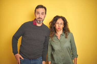 Soyutlanmış sarı arka planda, komik yüzlü güzel bir orta yaşlı çift. Havayla şişmiş ağız, çılgın bir ifade..
