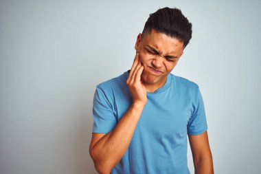 Mavi tişört giyen genç Brezilyalı adam diş ağrısı ya da diş ağrısı yüzünden izole edilmiş beyaz arka plan üzerinde durup ağız ve acı dolu yüz ifadelerine dokunuyor. Dişçi konsepti.