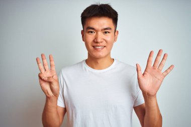 Asyalı genç bir Çinli tişört giyiyor. İzole edilmiş beyaz arka plan üzerinde duruyor. Sekiz numaralı parmaklarıyla işaret ediyor..