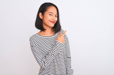Çizgili tişört giyen genç Çinli bir kadın izole edilmiş beyaz arka planda neşeli bir şekilde duruyor. Yüzünde mutlu ve doğal bir ifade olan, elleri ve parmaklarıyla yüzünü gösteren bir gülümseme var.