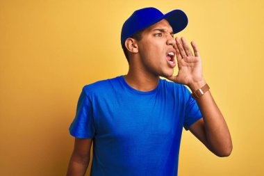 Genç yakışıklı Arap teslimatçı, izole edilmiş sarı arka planda durmuş el ele tutuşarak bağırıyor ve çığlık çığlığa bağırıyordu. İletişim konsepti.