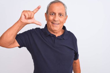 İzole edilmiş beyaz arka planda siyah polo giyen yaşlı gri saçlı adam gülümsüyor ve el hareketleriyle küçük boy işareti yapıyor, parmaklarıyla kameraya bakıyor. Ölçü kavramı.