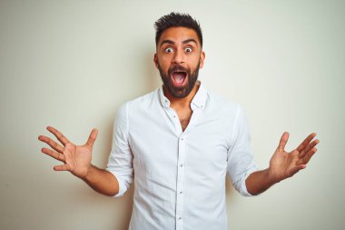 Zarif bir gömlek giyen genç Hintli adam izole edilmiş beyaz arka planda çılgın ve hayret verici bir başarıyı kollarını kaldırıp heyecanla haykırarak kutluyor. Kazanan konsept