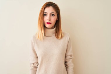 Sarışın, zarif balıkçı yaka kazak giyen, izole edilmiş beyaz arka planda duran, yüzünde ciddi bir ifadeyle rahatlamış bir kadın. Basit ve doğal bir şekilde kameraya bakıyorsun..