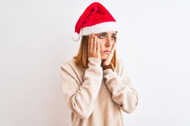 Güzel kızıl saçlı kadın, izole bir arka planda Noel şapkası takıyor. Yüzü, depresyonu ve üzüntüyü örten yorgun eller, sorun yüzünden üzgün ve sinirli.