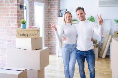 Genç ve güzel bir çift, yeni evlerinde karton kutuların etrafında dikilip kameraya gülümsüyor ve zafer işareti yapıyor. İki numara..