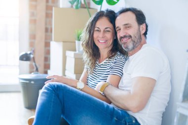 Orta yaş üst düzey romantik çift etrafında karton kutular ile daire katında oturan ve yeni bir eve taşınmak için mutlu gülümseyen aşk