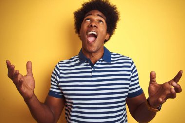 Afro saçlı, lacivert çizgili polo giyen Amerikalı adam izole edilmiş sarı arka planda çılgın deli bağırıyor ve agresif bir ifade ve kolla bağırıyor. Hayal kırıklığı konsepti.