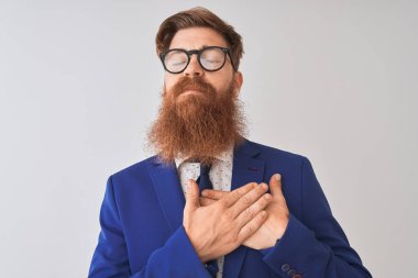 Genç kızıl İrlandalı işadamı kapalı gözleri ve yüzünde minnettar jest ile göğüs üzerinde gülümseyerek izole beyaz arka plan üzerinde takım elbise ve gözlük giyiyor. Sağlık kavramı.