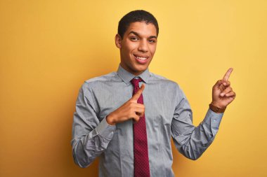 Yakışıklı Arap iş adamı gömleği ve kravat takıp izole edilmiş sarı arka planda gülümseyerek kameraya bakıyor ve iki eliyle ve parmaklarıyla yüzünü işaret ediyor..