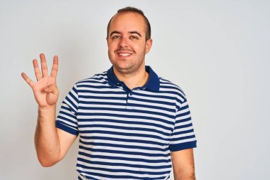 Sıradan çizgili polo giyen genç adam izole edilmiş beyaz arka planda duruyor ve dört numaralı parmaklarıyla işaret ederken kendinden emin ve mutlu bir şekilde gülümsüyor..