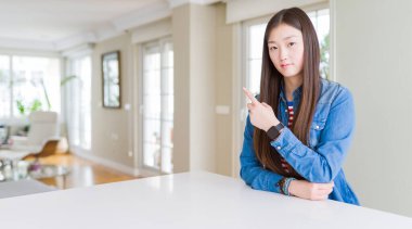 Uzun saçlı, güzel Asyalı kadın kot ceket giyiyor. El parmağı ile işaret ediyor. Reklam yapıyor, ciddi ve sakin bir yüz.