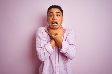 İzole edilmiş pembe arka planda dikilen Brezilyalı genç adam bağırıyor ve boğuluyor çünkü acı verici bir boğulma var. Sağlık problemi. Boğulma ve intihar konsepti.