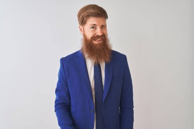 Genç, kızıl saçlı, takım elbiseli bir iş adamı izole edilmiş beyaz arka planda durmuş kameraya seksi bir ifadeyle bakıyor, neşeli ve mutlu bir yüzle..