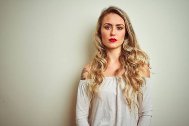 Yüzünde ciddi bir ifadeyle beyaz izole edilmiş arka planda duran genç ve güzel bir kadın. Basit ve doğal bir şekilde kameraya bakıyorsun..