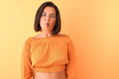 İzole edilmiş turuncu arka plan üzerinde duran sıradan tişört giyen genç ve güzel bir kadın dudaklı balık suratı yapıyor, çılgınca ve komik bir jest. Komik ifade.