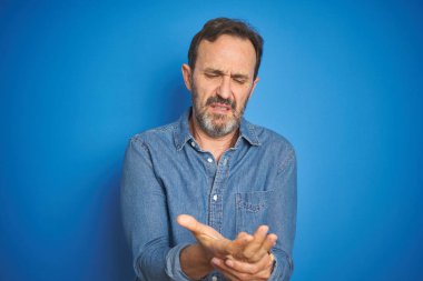 Yakışıklı, orta yaşlı, gri saçlı, soyutlanmış mavi arkaplan giyen, elleri ve parmakları ağrıyan, eklem iltihabı olan bir adam.