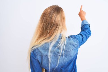 İzole edilmiş beyaz arkaplanın üzerinde duran sıradan bir kot gömlek giyen genç ve güzel bir kadın geriye doğru poz veriyor.